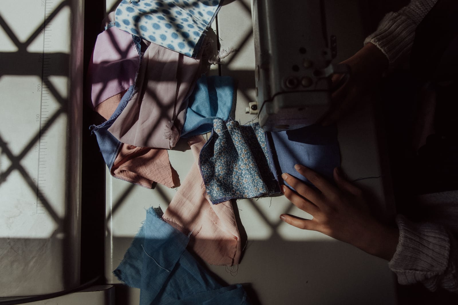 Hands guiding salvaged fabric through a sewing machine in afternoon light
